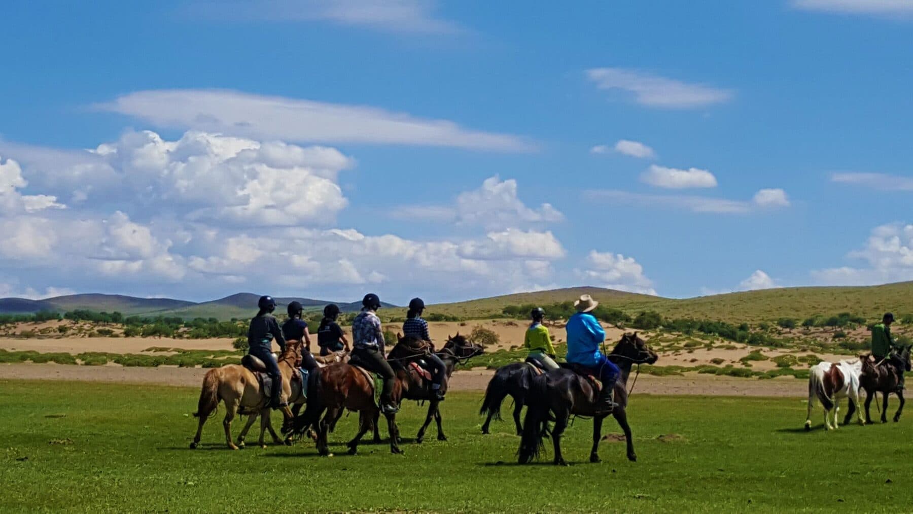 Riders crossing green steppe under a blue sky