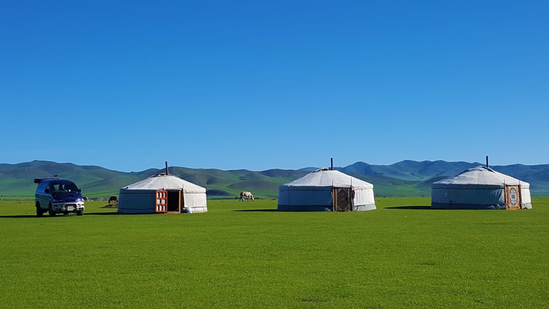 Three gers on open steppe under a blue sky