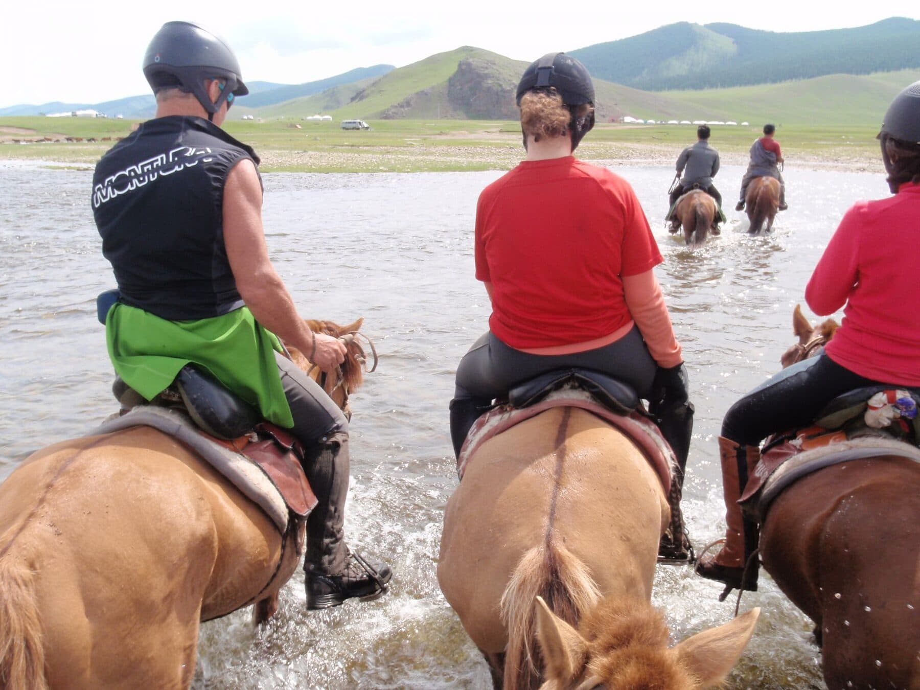 Riders crossing a river toward green hills
