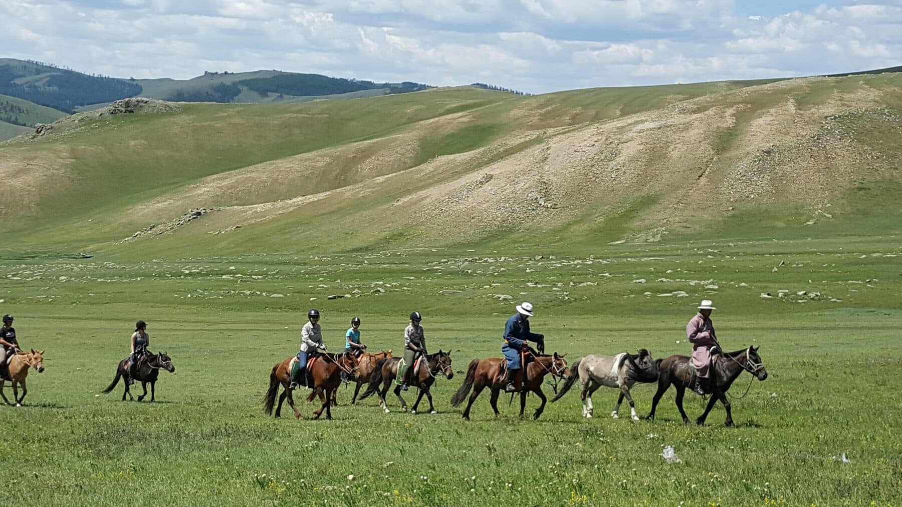 Riders crossing green steppe below rolling hills