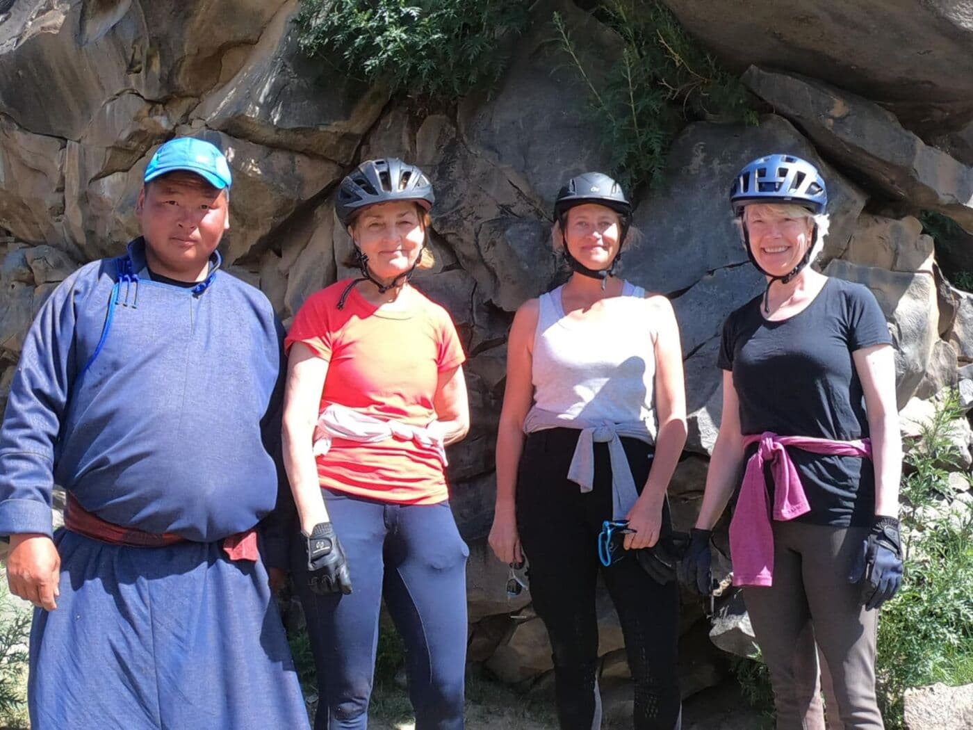 A Nomad Rider guide in a traditional deel with three riders in front of a rock face